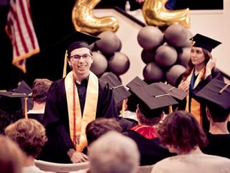 Students standing in audience for recognition, man standing at podium on stage