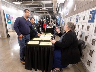 A staff member is conversing with two parents at a table