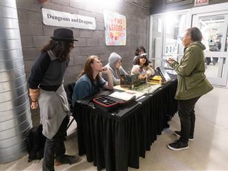 A staff member is engaging with 5 students at their table display