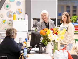 A parent and student are seen talking with a teacher at their desk