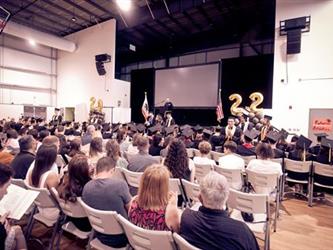 Students standing in audience for recognition, man standing at podium on stage