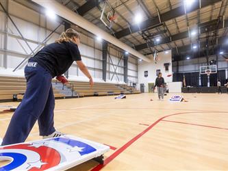 Two students are seen playing cornhole in gymnasium