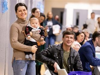 Woman with infant standing and man sitting smiling at camera