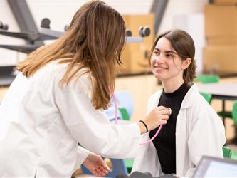 A student is using a stethoscope on another student